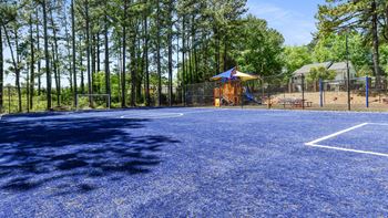 a basketball court with a playground in the background and trees at 300 Riverside Apartments, Austell, Georgia